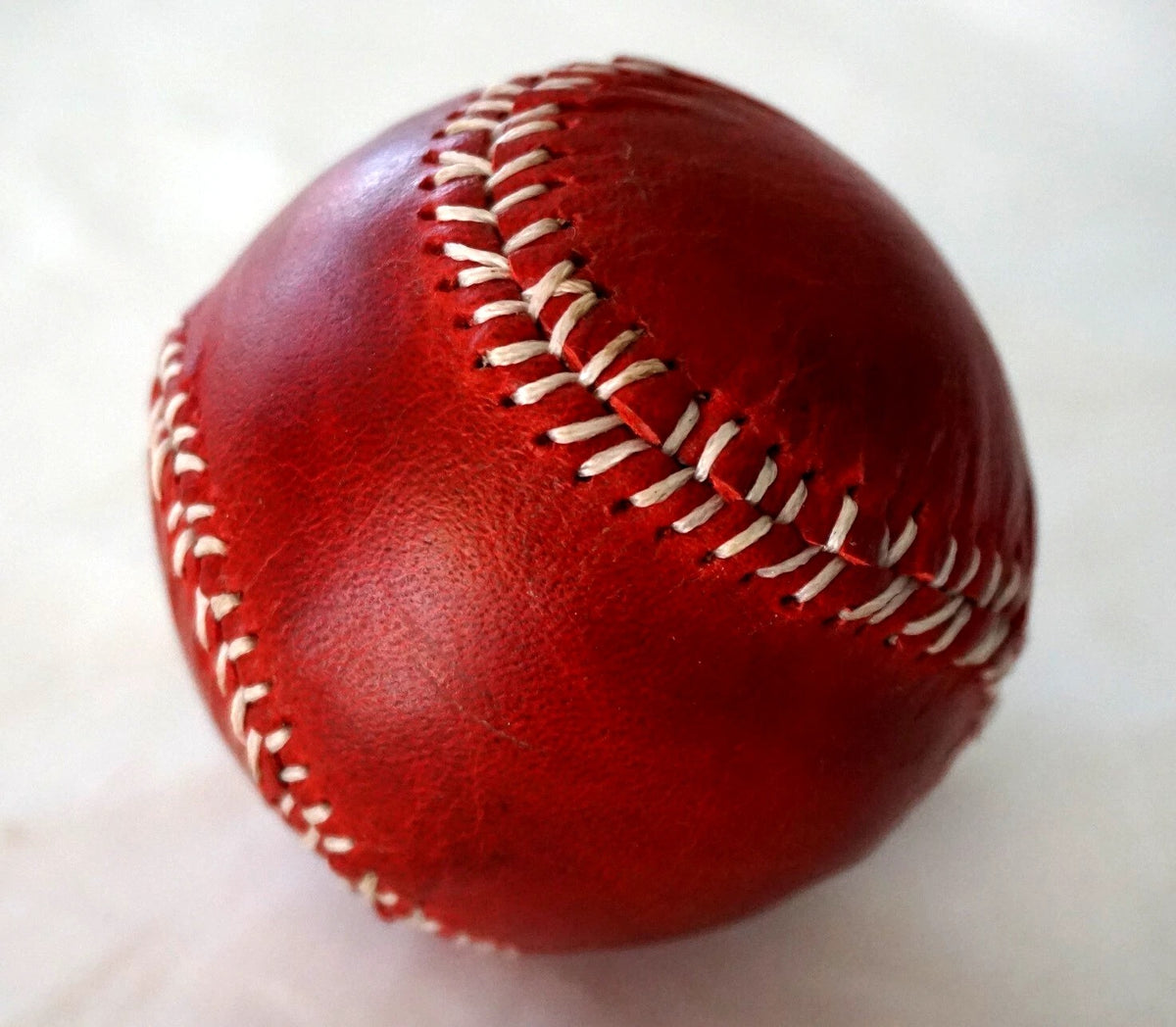 Handmade vintage red leather baseball with sewing thread and needle, crafted by DAVISCASE, showcasing detailed stitching and craftsmanship.