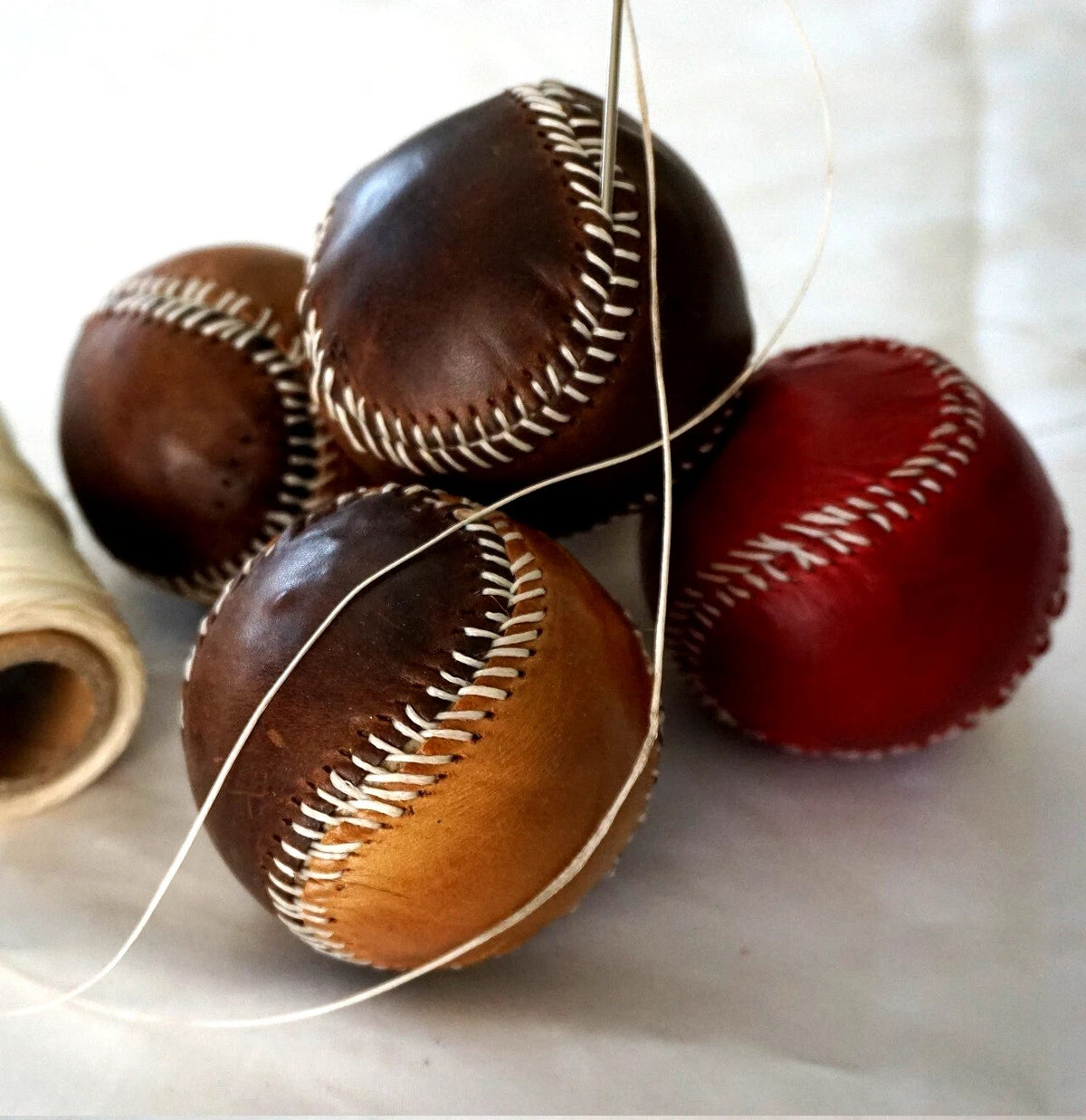 Handmade red leather baseball with stitching, crafted by DAVISCASE, featuring thread and needle for vintage-style sewing.